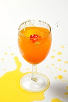 A dice falling into a glass of orange liquid caused a splash. Close up on white background