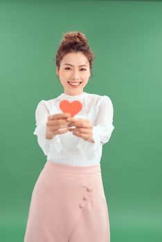 Cheerful young Asian woman holding red heart paper isolated over green background. 