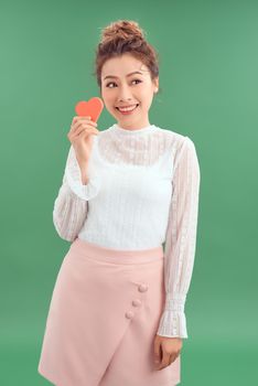 Asian Woman holding paper heart shaped card over green background. Valentine day concept.