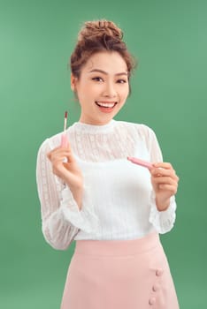 Cheerful young Asian woman applying lipstick isolated over green background.