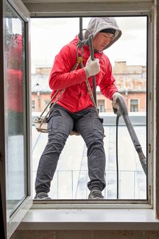 A window washer in climbing gear hangs in the window opening, seen from inside the building