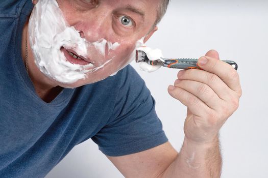 A man's face in shaving foam shaves with a safety razor. Morning or evening exercise, personal hygiene