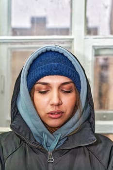 Facial portrait of a pretty girl in a hat and dark jacket with a hood looking at the camera