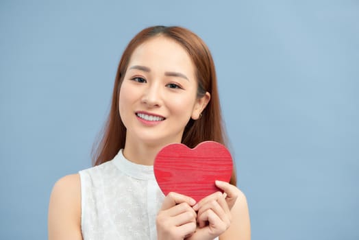 Happy woman hold red heart. Beautiful female model posing on isolated blue background.