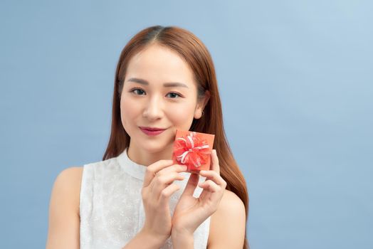 Cheerful young woman holding small gift box isolated on a blue background