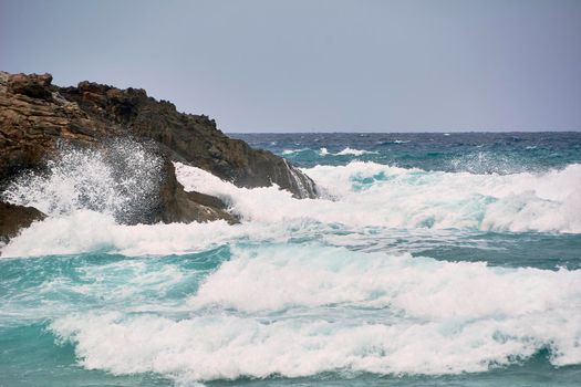 Rocks on the shore hit by the waves. Balearic Islands, Mediterranean Sea, blue sky, splashes of water.