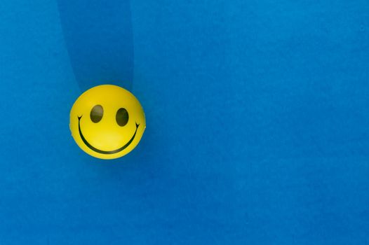 Anthropomorphic smiley face expression of a Squeeze Ball or Stress Ball isolated on blue background. Table top view. Close up. Happy smile background concept.