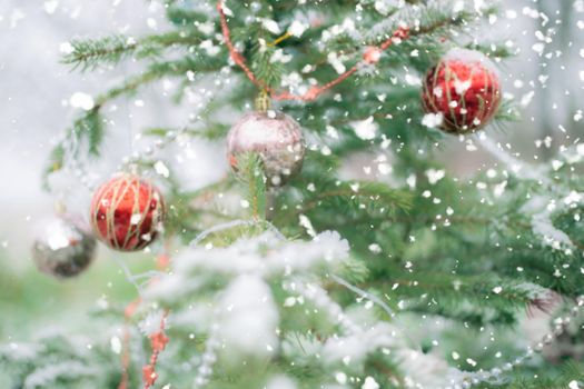 Blurred, defocused christmas tree background with holiday decorations and snow falling outside in winter.