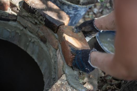 A worker lays the mouth of a septic well out of bricks. Work with cement.