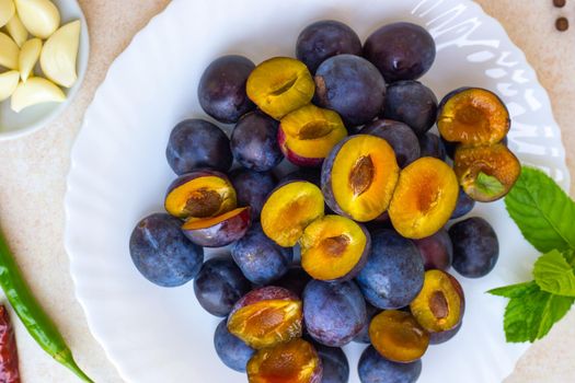 Cooking spicy plum sauce. Ingredients for tkemali on the table plate with plums, seasonings, close-up.