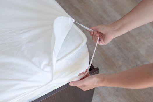 The woman makes the bed, putting on a protective waterproof cover on the mattress. Clean linen and comfortable sleep.