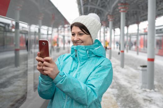 Woman writes sms on cell phone at railway station in winter during snowfall in Moscow, Russia