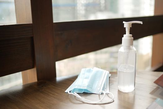 Surgical masks, and hand sanitizer on table against a window .