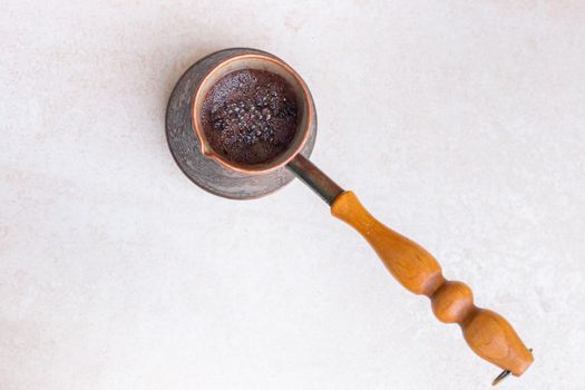 Freshly brewed black coffee in a metal turk on a light table, top view. Morning invigorating drink.