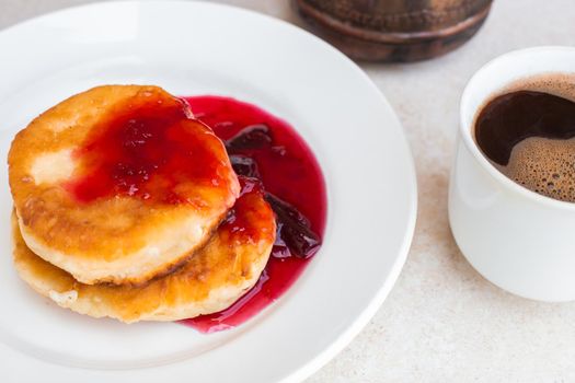 Fresh cheesecakes with plum jam and a mug with freshly brewed coffee on a light tabletop. Wake up in the morning, start a new day. Hearty breakfast.