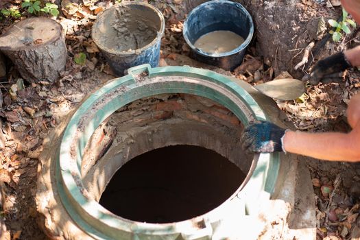 Laying a hatch on a sewer well. The man strengthens the neck of the septic tank.