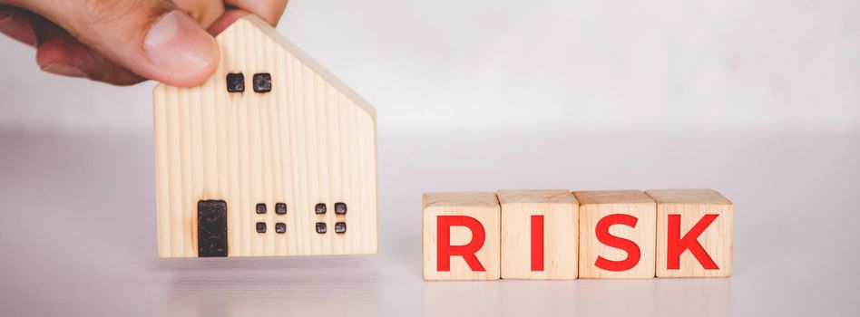 Planning with finance and investment of business about real estate with risk and safety of insurance, uncertainty for economy, hands put home and cube wooden block with word RISK, business concepts.