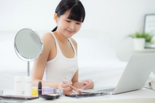 Beauty of young asian woman with learning makeup with brush on cheek on laptop computer with tutorial course online, female teaching and explain make up with cosmetic on streaming social media.