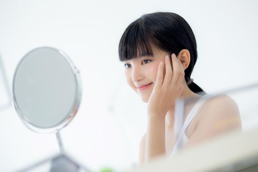 Beautiful face of young asian woman with happy smiling and touch cheek looking mirror with charming, makeup of beauty facial girl with skincare and cosmetic treatment, skin care and healthy concept.