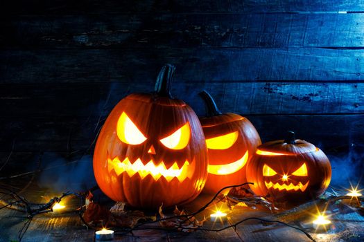 Halloween pumpkins head jack o lantern, candles and dry maple leaves in mist