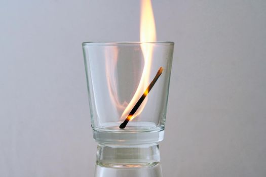 Burning match in a transparent glass on a light background. Concept, symbol