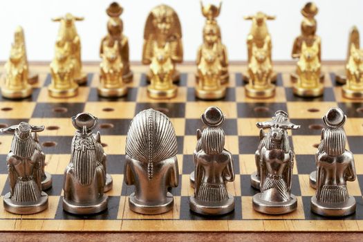 Chess board with placed chess pieces stylized as Egyptian gods. Focus on silver pieces