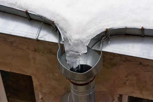 Melting ice and snow on the roof at the drainpipe. Close up