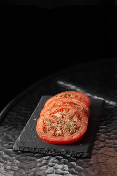 Sliced ​​tomatoes with herbs. Black cutting board.