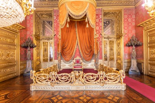 Turin, Italy - Circa August 2021: old throne room interior with chair in luxury palace. Red and gold antique Baroque style - Savoia Royal Palace