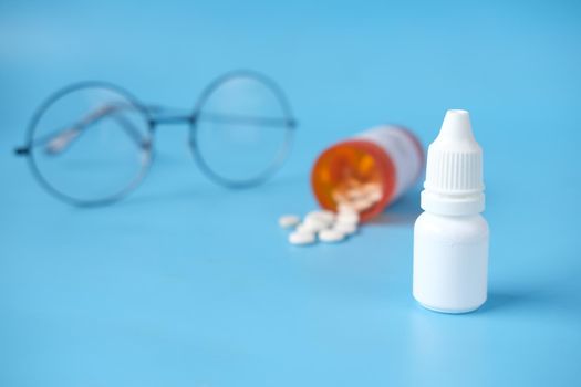 close up of eye drop bottle and eyeglass on white