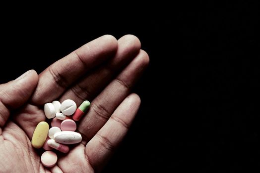 drug abuse concept with many pills on hand against black background .