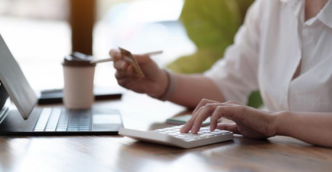 Woman accountant working in office using calculator and holding credit card, hands closeup, panoramic banner. Online shopping concept..