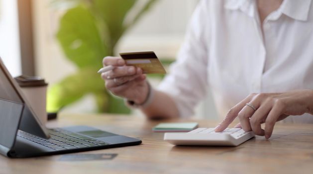 Woman making calculations and shopping online with credit card. Female using calculator, budget and loan paper in office. Bills, home budget, tax, savings, finances, economy, audit, debt concept.