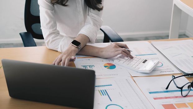 The hand of Asian woman is pressing calculator and prepare information for report to correct. While still holding a silver pen in finger. When calculated completed, can be recorded immediately..