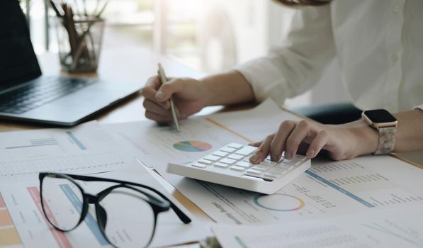 The hand of Asian woman is pressing calculator and prepare information for report to correct. While still holding a silver pen in finger. When calculated completed, can be recorded immediately..