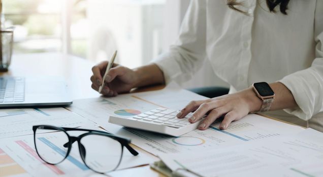 The hand of Asian woman is pressing calculator and prepare information for report to correct. While still holding a silver pen in finger. When calculated completed, can be recorded immediately..