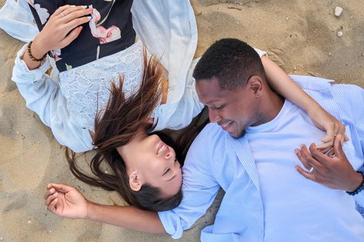 Top view of young multiracial couple in love. African american man and asian woman lying together on the sand. Love, relationship, lifestyle, dating, multiethnic family, happiness concept