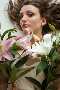 Top view of beautiful woman lying on the table with perfect bouquet of beautiful lilies, female portrait concept.