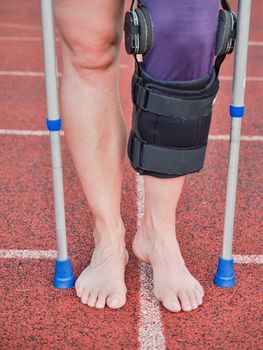 Woman suffering with walk by sticks and knee brace support surgery left knee in recovery time.