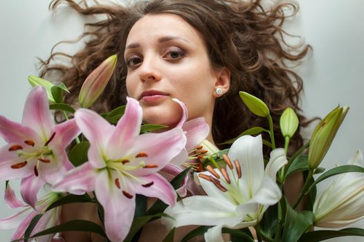 Top view of beautiful woman lying on the table with perfect bouquet of beautiful lilies, female portrait concept.