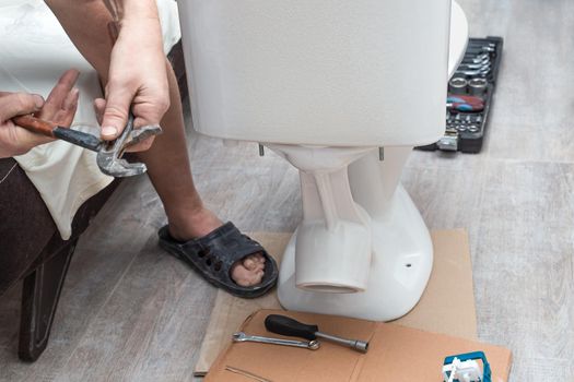 Plumbing installation. A man installs a toilet cistern on a toilet seat.