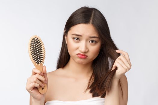 Upset stressed young Asian woman holding damaged dry hair on hands over white isolated background