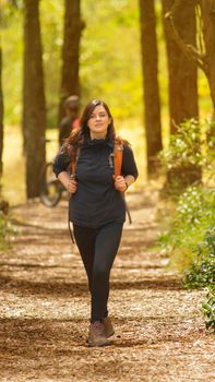 Beautiful Hispanic woman dressed in black with backpack walking alone on a forest path during the morning