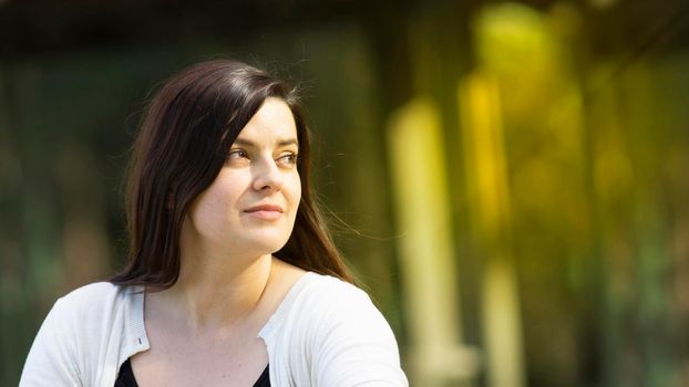 Portrait of beautiful Hispanic young woman with long hair looking to the right against a background of unfocused trees during sunset with copy space