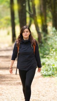 Beautiful Hispanic woman with backpack walking alone on a forest path during the morning