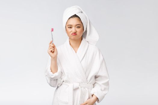 Unhappy beautiful woman brushing her teeth on white background.