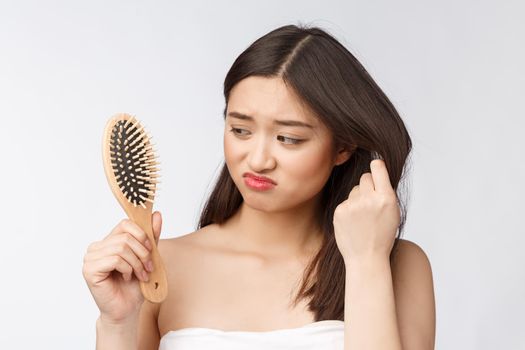 Upset stressed young Asian woman holding damaged dry hair on hands over white isolated background