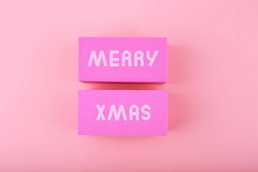 Trendy pink Merry Xmas minimal concept in light colors. Text Merry Christmas on pink tablets against light pink background. 