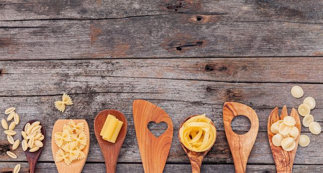 Italian foods concept and menu design . Various kind of pasta elbow macaroni ,farfalle ,rigatoni ,gnocco sardo in wooden spoons setup on wooden background.