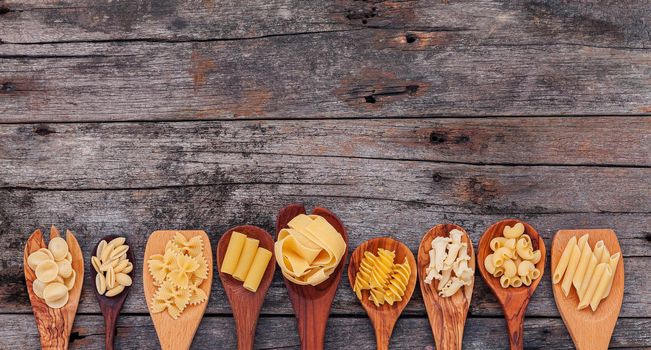 Italian foods concept and menu design . Various kind of pasta elbow macaroni ,farfalle ,rigatoni ,gnocco sardo in wooden spoons setup on wooden background.